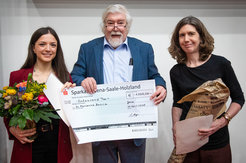 Award winner Marianna Boccia with a bouquet of flowers, Wilhelm Boland with a large check containing the prize money, and Sarah O'Connor.